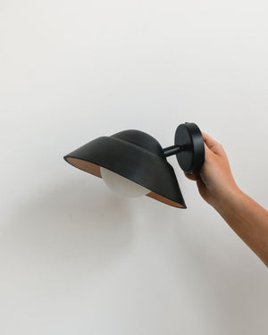Hand holding black leather wall light with adjustable arm against beige background