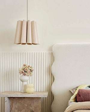 Decorative lampshade hanging above a table with a vase and flowers against a neutral wall.
