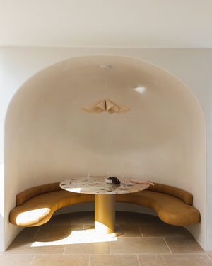 Modern interior design with a curved wall and built-in seating around a round table, featuring a wooden pendant.