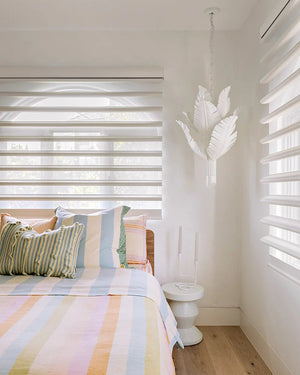 Bedroom with colorful striped bedding and banana leaf pendant.