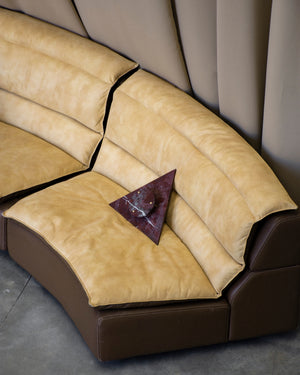 Beige sectional sofa with a brown base an a triangular marble wall light