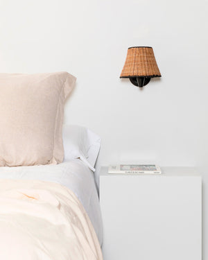 Black and Natural Rattan Wall Light Light Off Beside a Bed