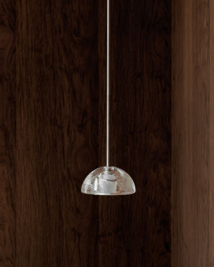 Small pendant light with a textured glass shade hanging against a wooden background
