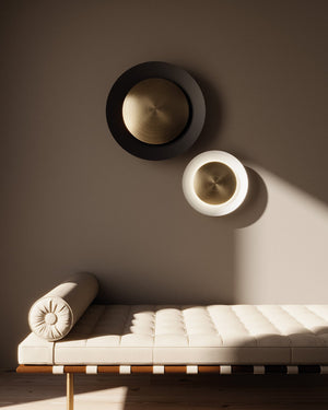 Two wall-mounted circular lights on a beige wall with a bench below.