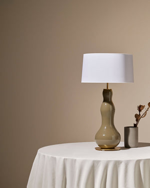 Decorative table lamp with a white shade on a round table against a beige wall.