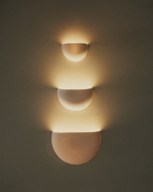 Wall-mounted light fixture with three spherical shades on a plain wall.