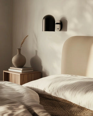 Bedroom scene with a vase on a nightstand and Curved Matte Black Wall Light casting shadows.