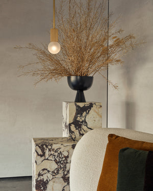 Decorative vase with dried plants and a pendant light in a modern interior setting.