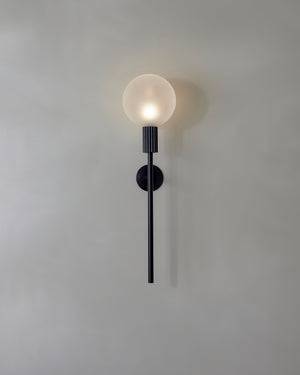 Wall-mounted light fixture with a round glass shade on a plain wall.
