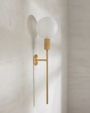 Brass wall sconce with a white bulb on a light gray wall light off