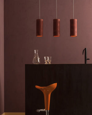 Three pendant lights hanging above a bar counter with a brown wall background.