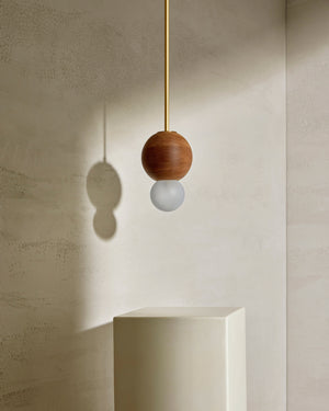 Modern pendant light with wooden shade and white bulb against a neutral wall.