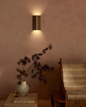 Wall-mounted light fixture casting a warm glow on a wall with a vase and plant on a table.