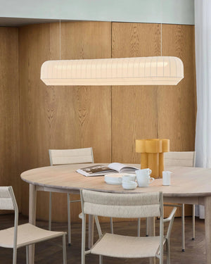 Dining area with a round table, chairs, and a Knitted Stretched Fabric Linear against a wooden paneled wall.