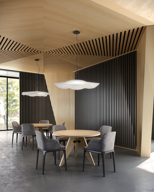 Modern dining area with round table and gray chairs in a room with wooden ceiling and black striped walls.