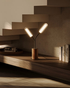 Modern table lamp with three light bulbs on a wooden shelf next to books.