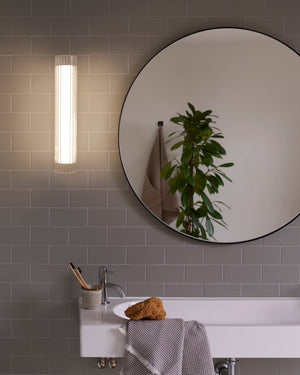Fluted Glass Cylindrical Wall Light beside a round bathroom mirror