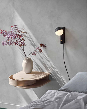 Modern wall light fixture with a vase and branches on a wooden shelf against a gray wall.