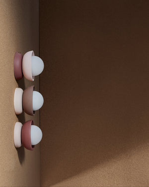 Three ceramic Mani wall sconces on a brown surface with a dark brown background