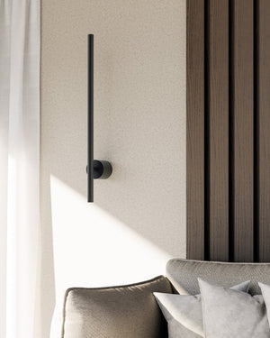 Modern black wall-mounted lamp against a neutral wall with a bed in the foreground