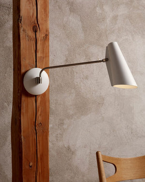 Mid-Century Style Swing Arm Wall Light with white shade and gold arm on a textured wall.