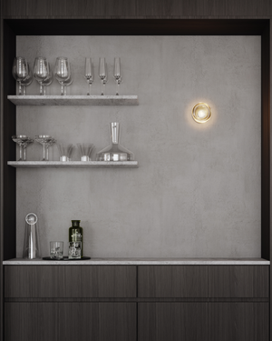 Modern kitchen bar setup with shelves, glasses, and a light fixture on a gray wall.