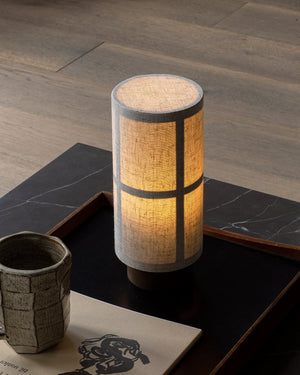 Cylindrical table lamp with woven design on a wooden surface