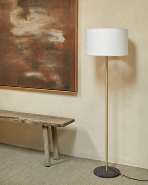 Minimalist Marble Floor Lamp with white shade and gold base next to a wooden bench and abstract painting on a beige wall.