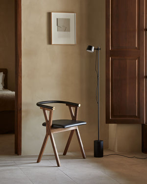 Chair with black cushion and wooden frame in a room with a Minimalist Matte Black Round Floor Lamp and wall art.