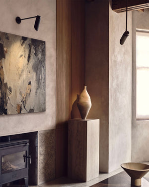 Modern interior with a vase on a pedestal next to a fireplace and abstract art minimalist wall light