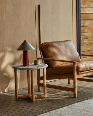 Iron base table lamp with tapered shade on marble table next to leather chair