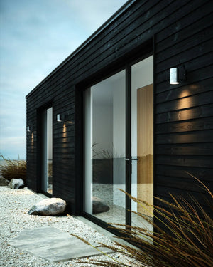 Modern black wooden house with large Steel exterior lights next to a beach