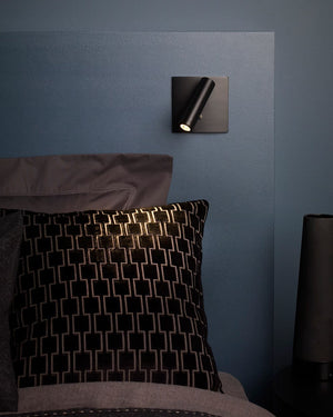 Modern wall light fixture on a blue wall above a bed with decorative pillows.