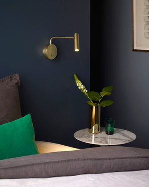Modern interior with a brass wall lamp, green vase, and gray bench against a dark blue wall.