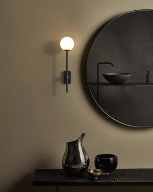 Modern bathroom setup with round mirror, wall light, and black fixtures.