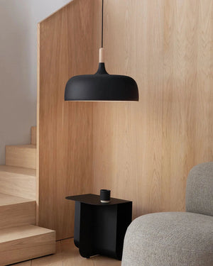 Modern black pendant light hanging above a staircase with wooden walls and a gray sofa.