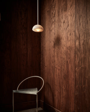 Pendant light fixture hanging above a chair against a wooden wall.