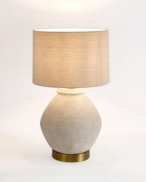 Table lamp with beige shade and textured white base on a light gray background