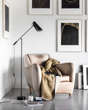 Modern living room with a beige armchair, Scandinavian designed floor lamp, and framed artwork on the wall.