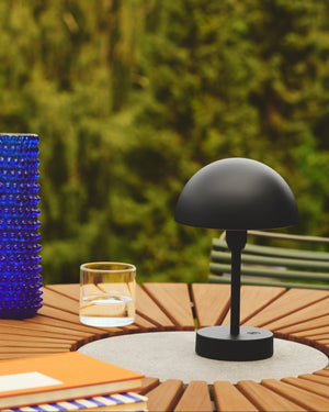 Black outdoor table lamp on a wooden table with a blurred green garden background