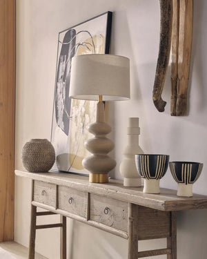 Decorative table with lamp, vases, and bowls against a wall with abstract art.