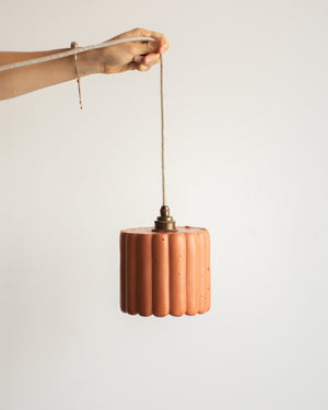 Terracotta pendant light held by a hand against a plain background