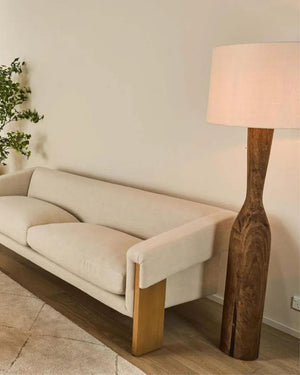 Beige sofa with wooden legs in a room with a wooden floor and a tapered timber floor lamp