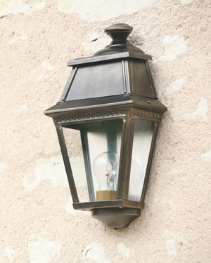 A classic french outdoor wall lantern light fixture with clear glass panels, mounted on a textured wall