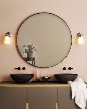 Bathroom vanity with round mirror, two black sinks, and wall lights on a beige wall.