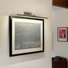 Framed artwork on a wall with a light fixture above it