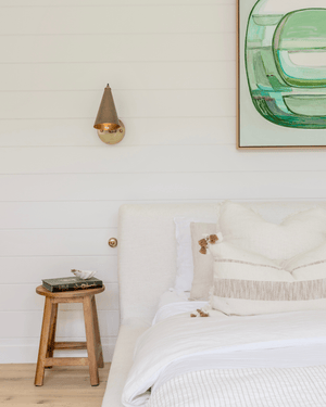 A-Frame Project: A modern brass cone wall sconce and a small wooden stool in a contemporary bedroom.