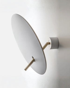 A modern wall-mounted light fixture with a large oval white shade and slim brass-toned metal arm, shown against a plain white wall.