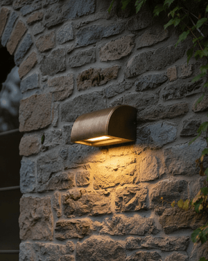 A modern curved outdoor wall light fixture in an antique bronze finish, mounted on an exterior wall