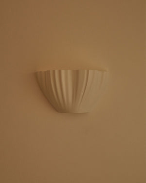 Semicircular wall light with an organic shape and textured folds on beige background